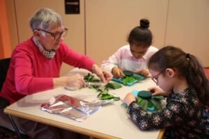 Une dame âgée et deux jeunes filles en train de faire un atelier de centre de table floral